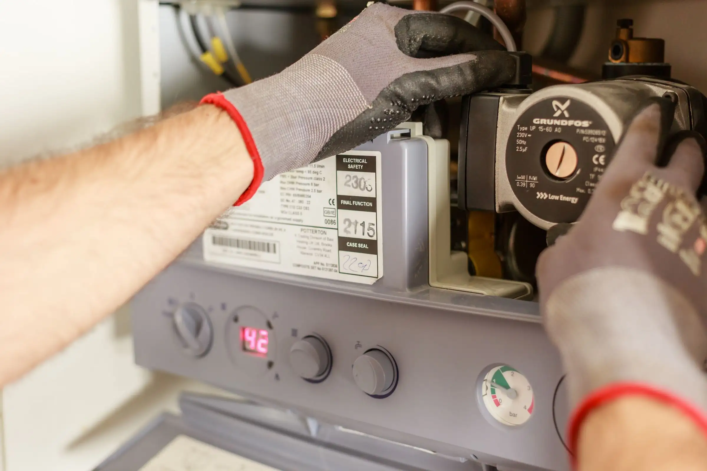 Hands adjusting a boiler control panel beside pressure gauges