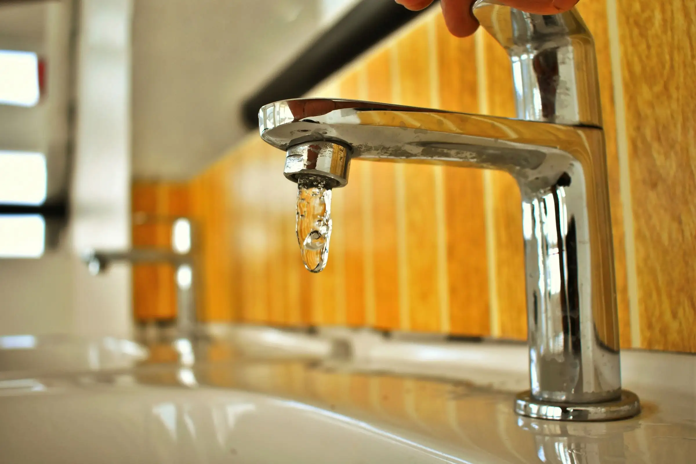 Chrome faucet holding a single drop at the spout