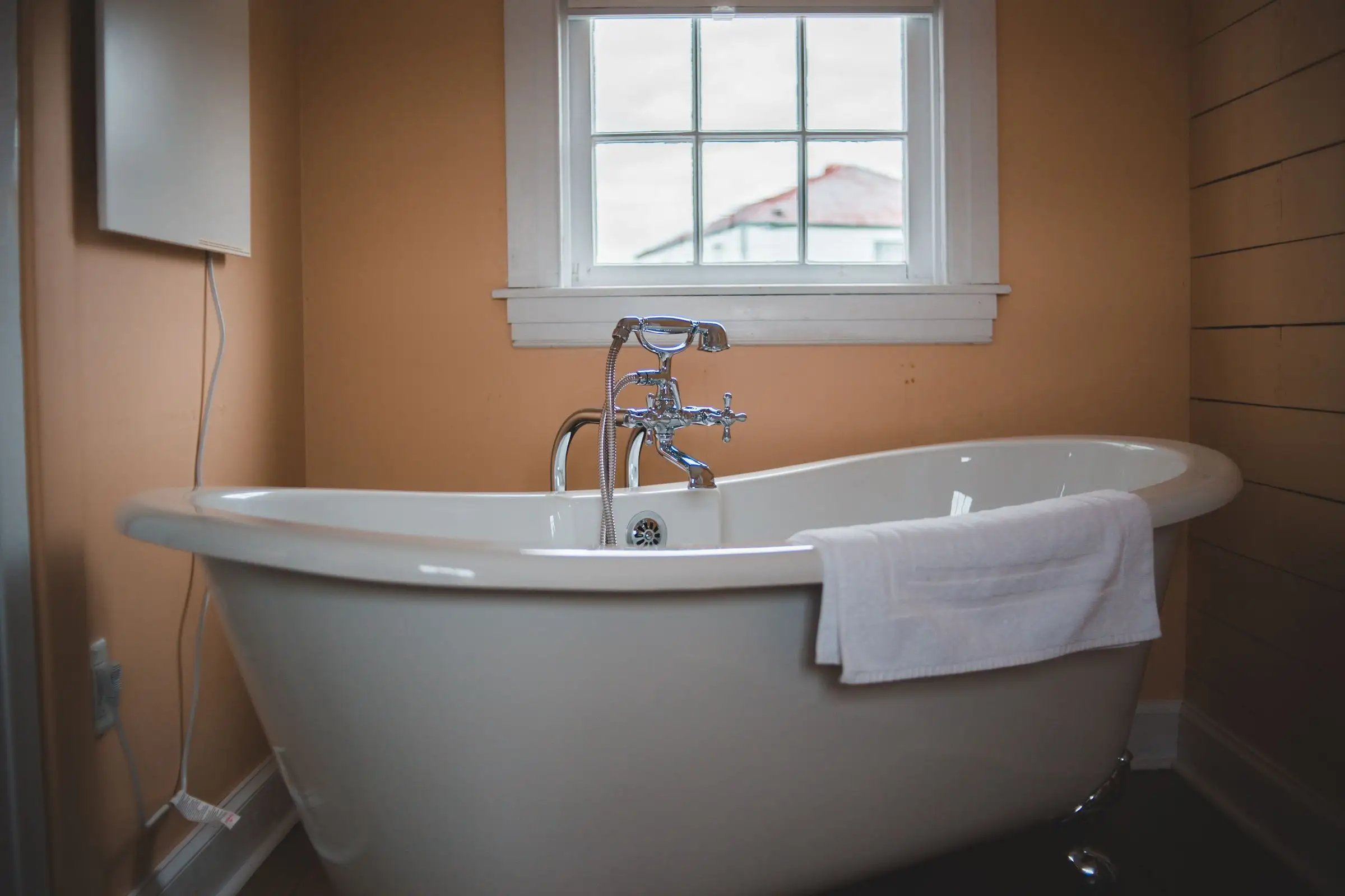 Clawfoot bathtub standing under a window in a plain bathroom