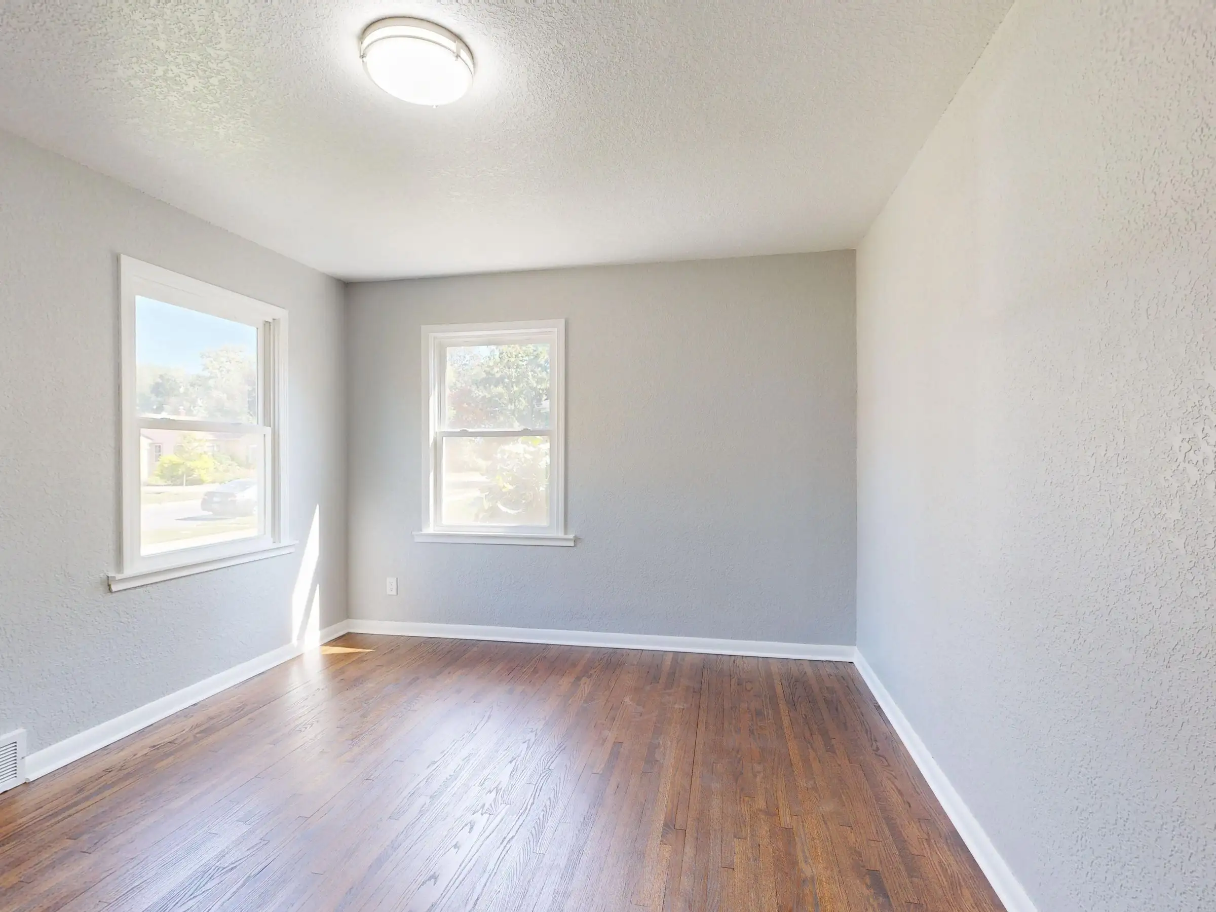 Empty room with hardwood floor lit by two tall windows