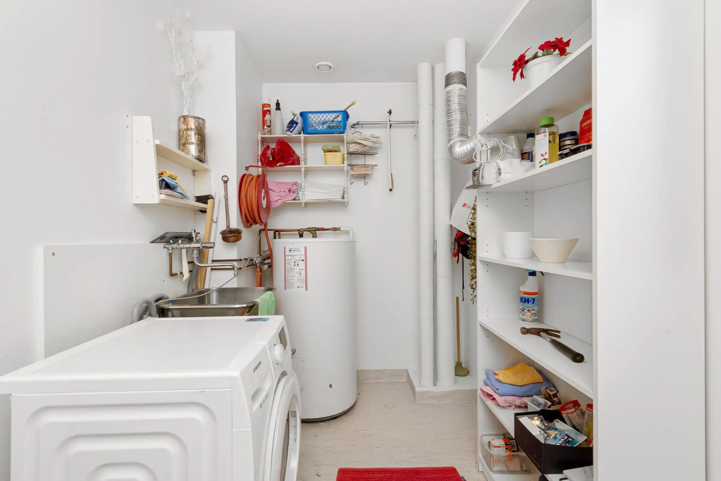 Laundry room with a washing machine and a water heater standing beside open shelving