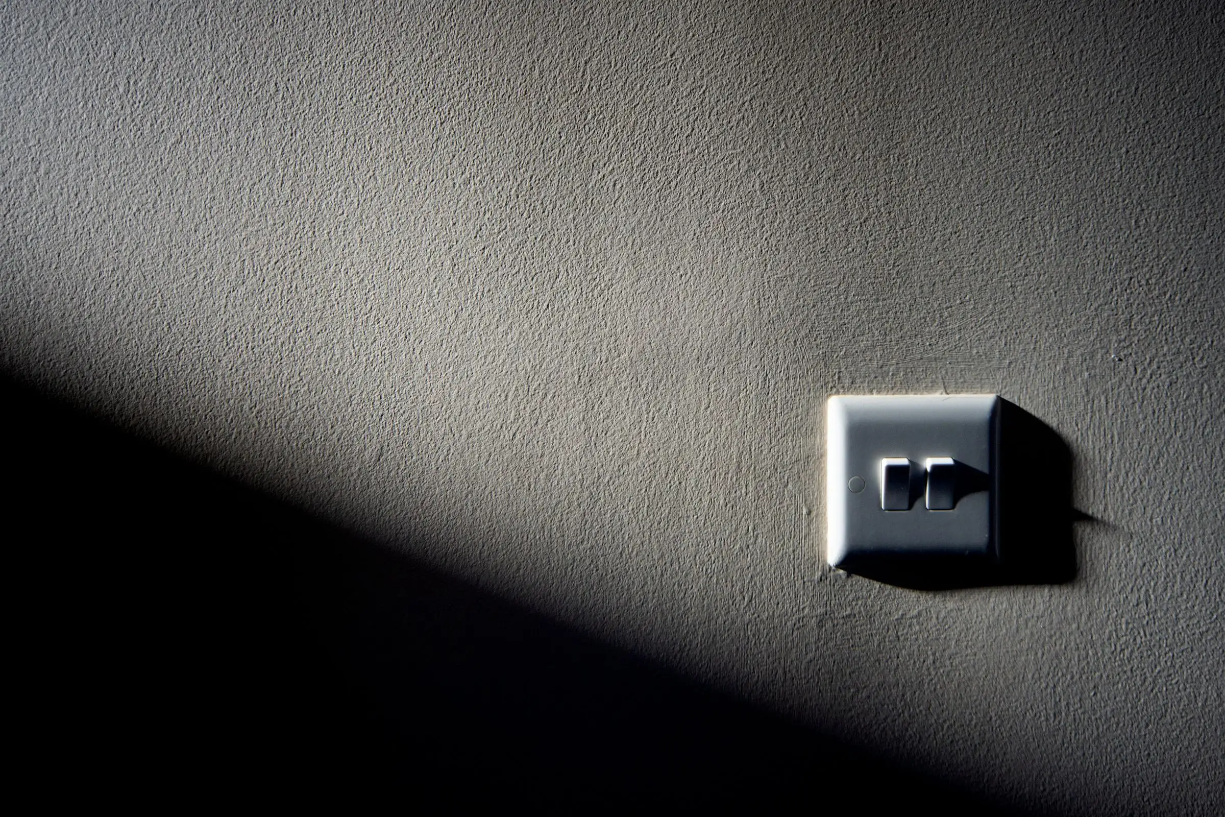 A light switch on a textured wall, lit from one side