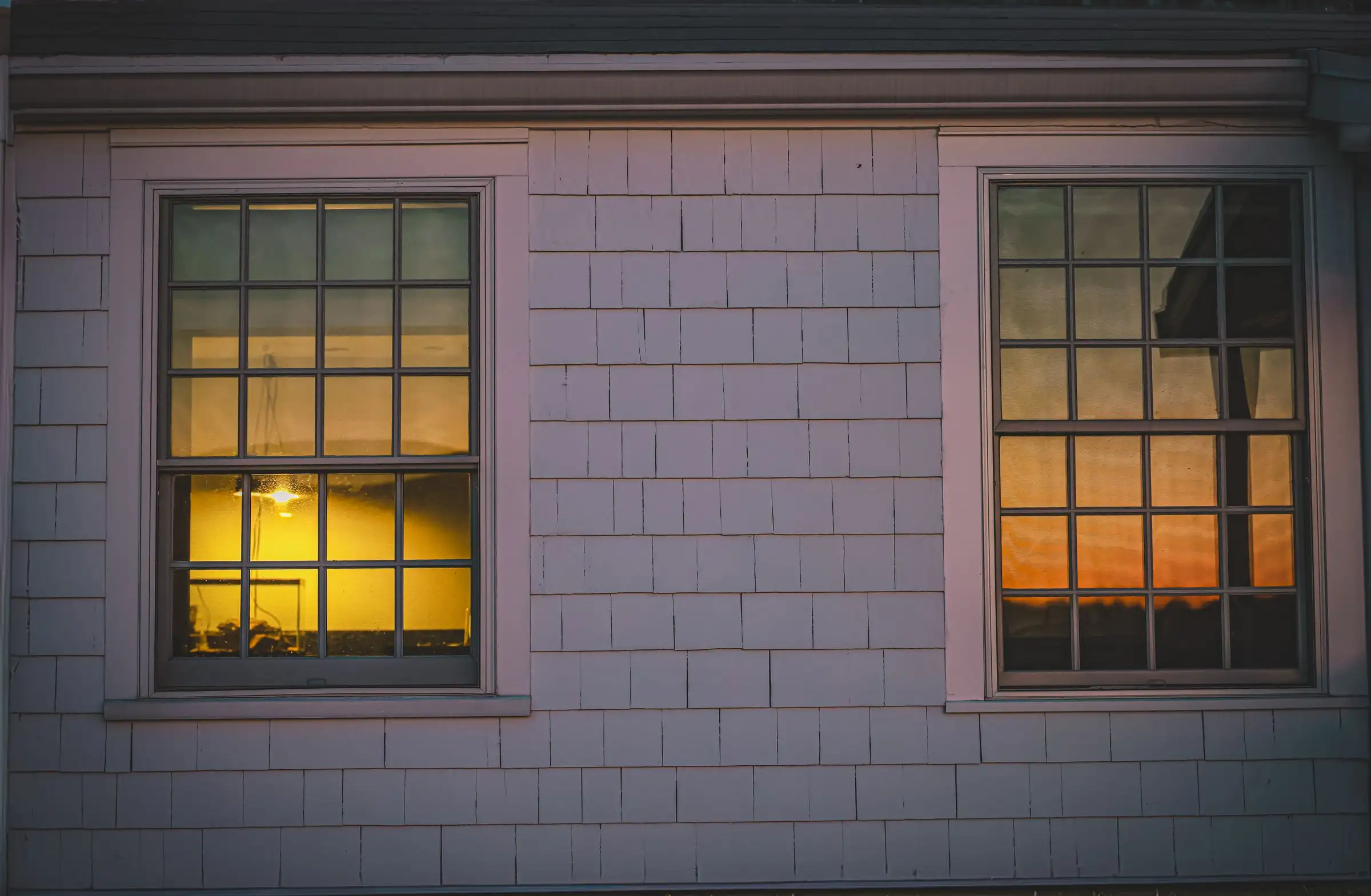 Lit windows of a house reflecting a twilight sky