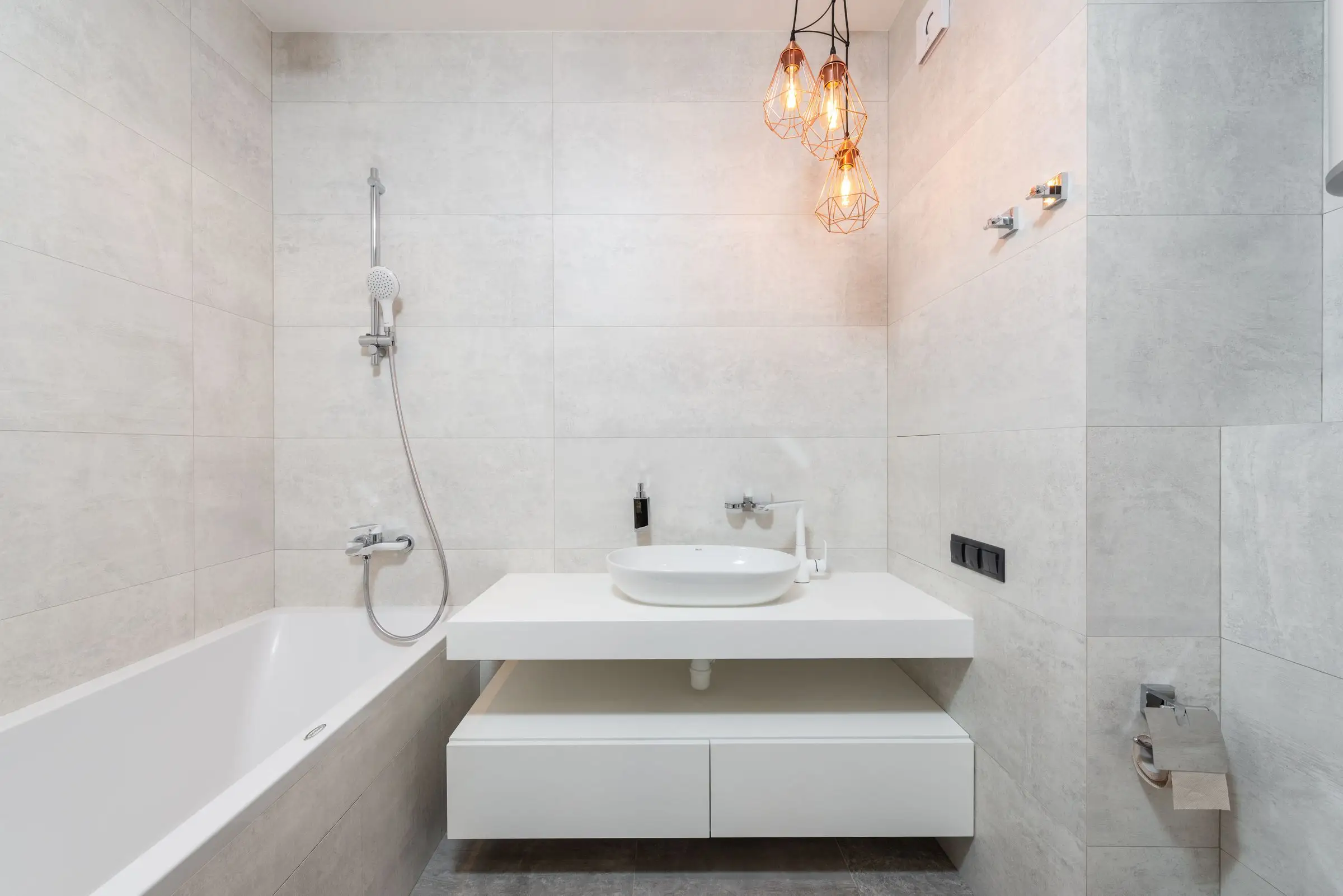 Bathroom lined in pale marble tile with a plain vanity and a wall mirror