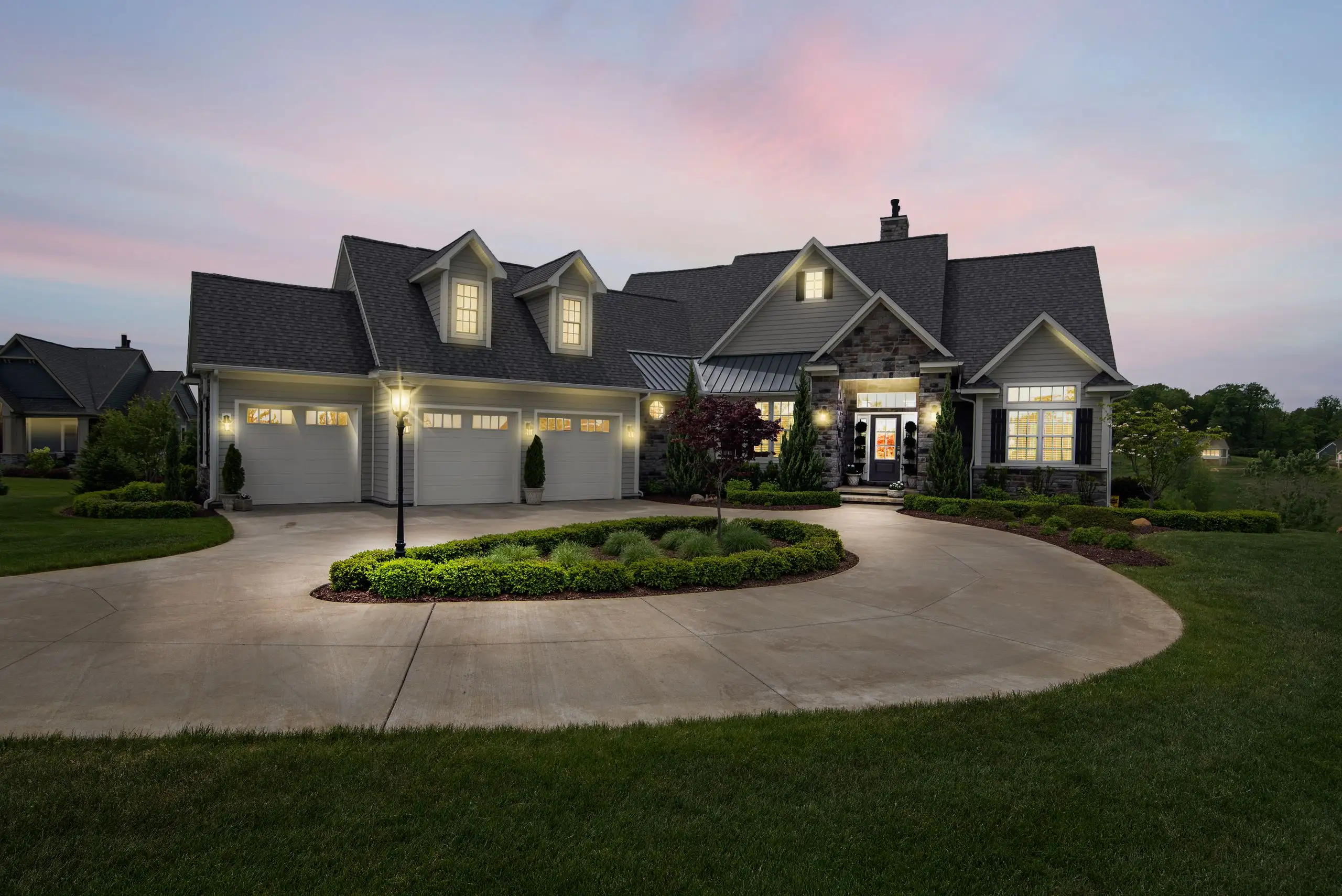 Suburban house lit at dusk, standing seam metal roof over the entry and stone-faced gable