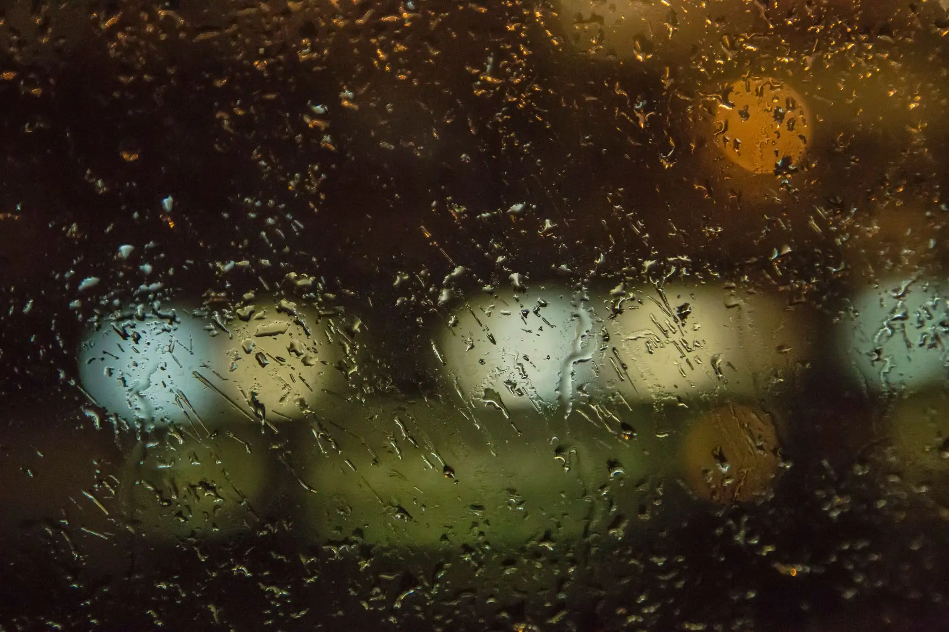 Rain streaking down a dark window pane at night, lights blurred beyond the glass
