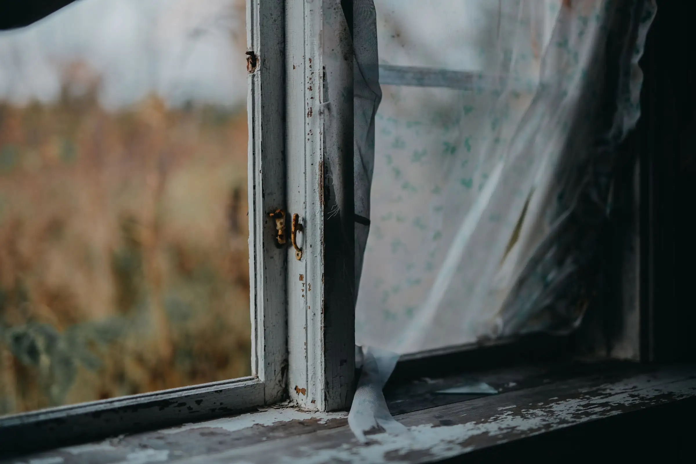 Old wooden window frame with peeling paint and bare timber showing at the sill