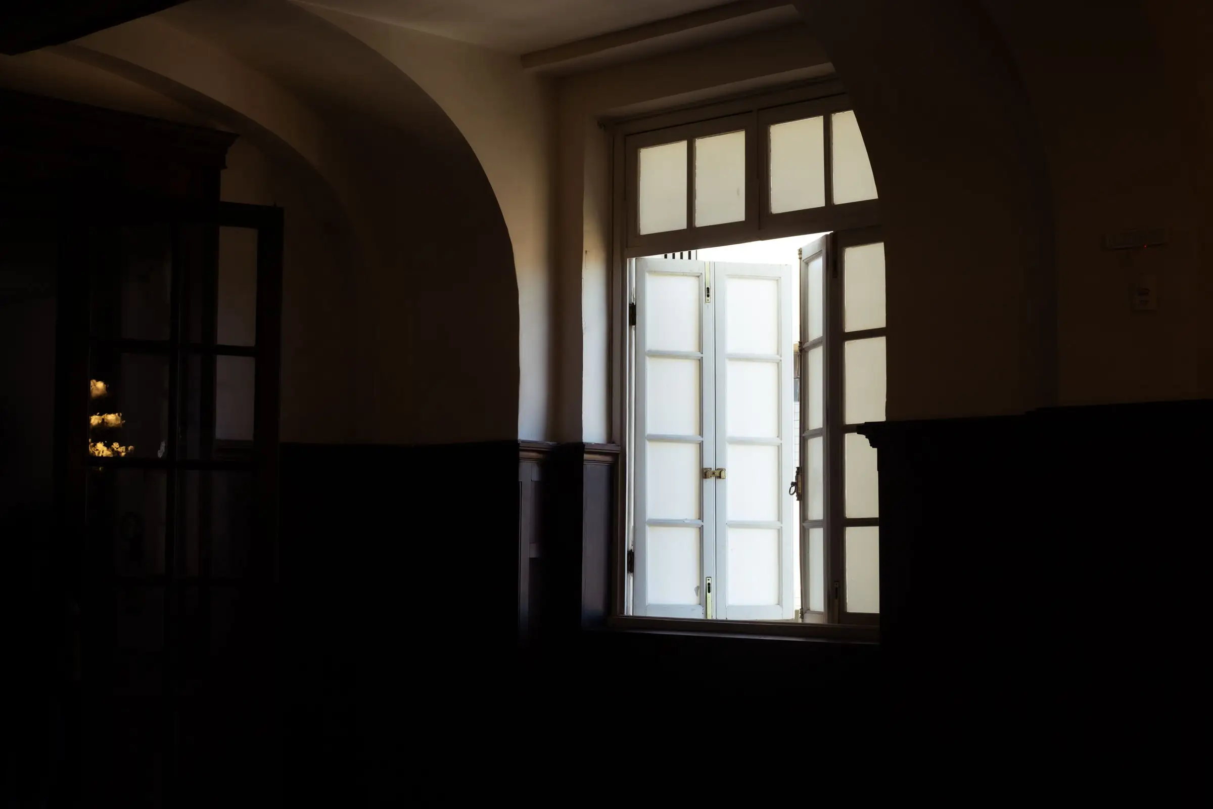 A single white-framed window standing open in a dark, bare room