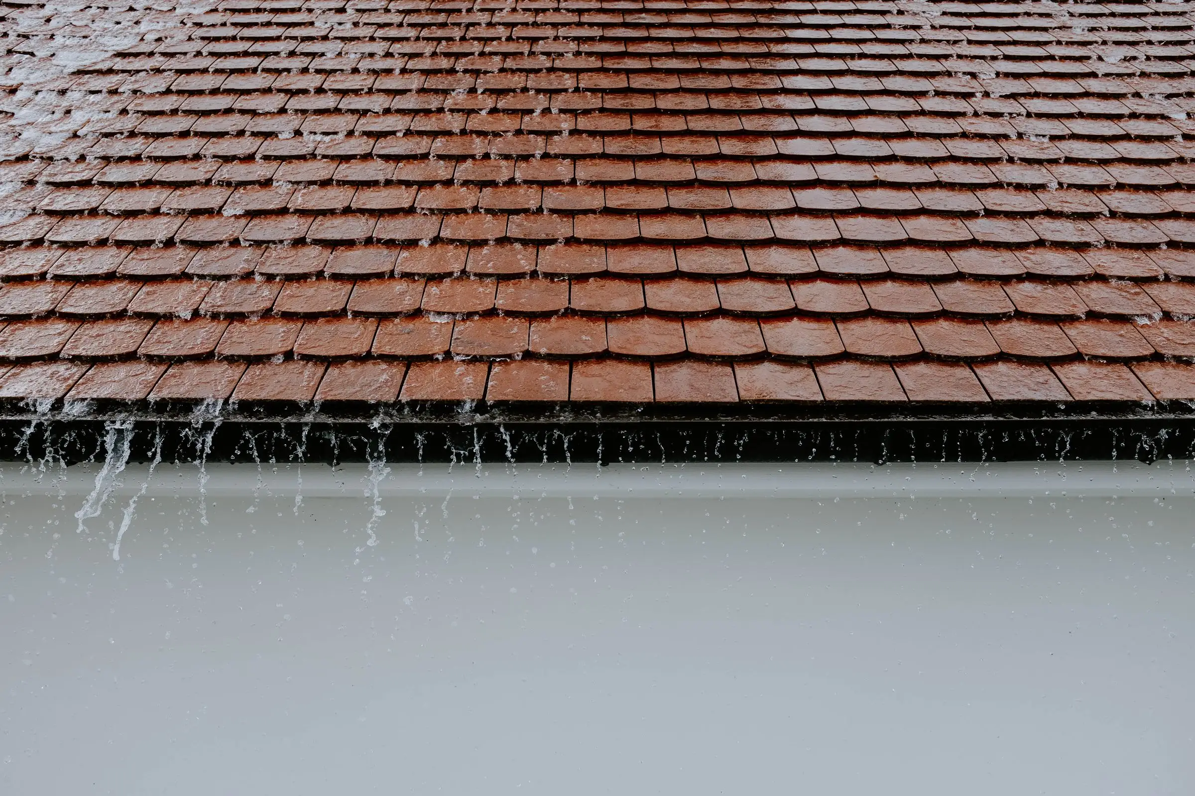 Rain sheeting off a tiled roof edge in heavy weather