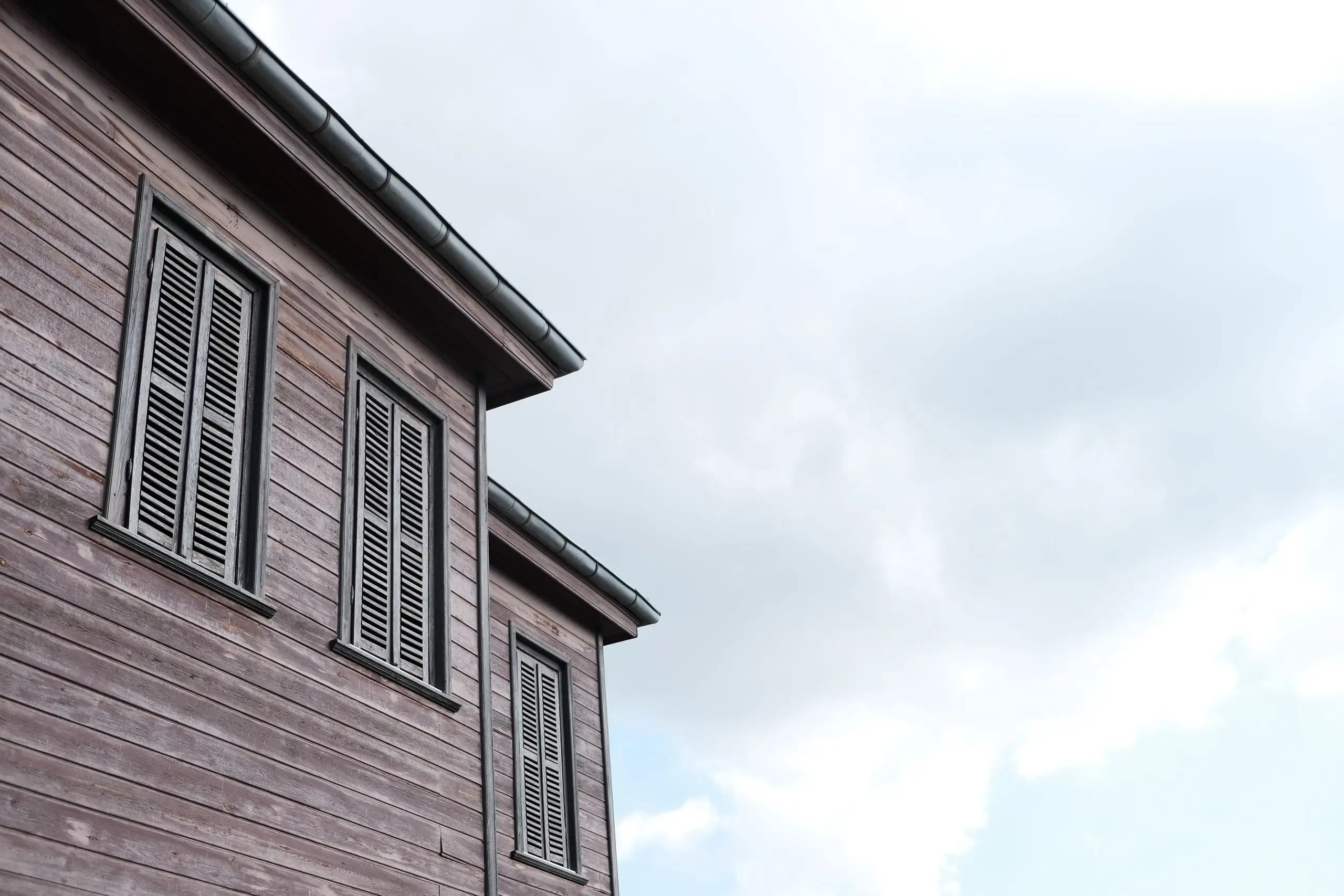 Roof edge and gutter of a weathered clapboard house seen from directly below against a pale sky