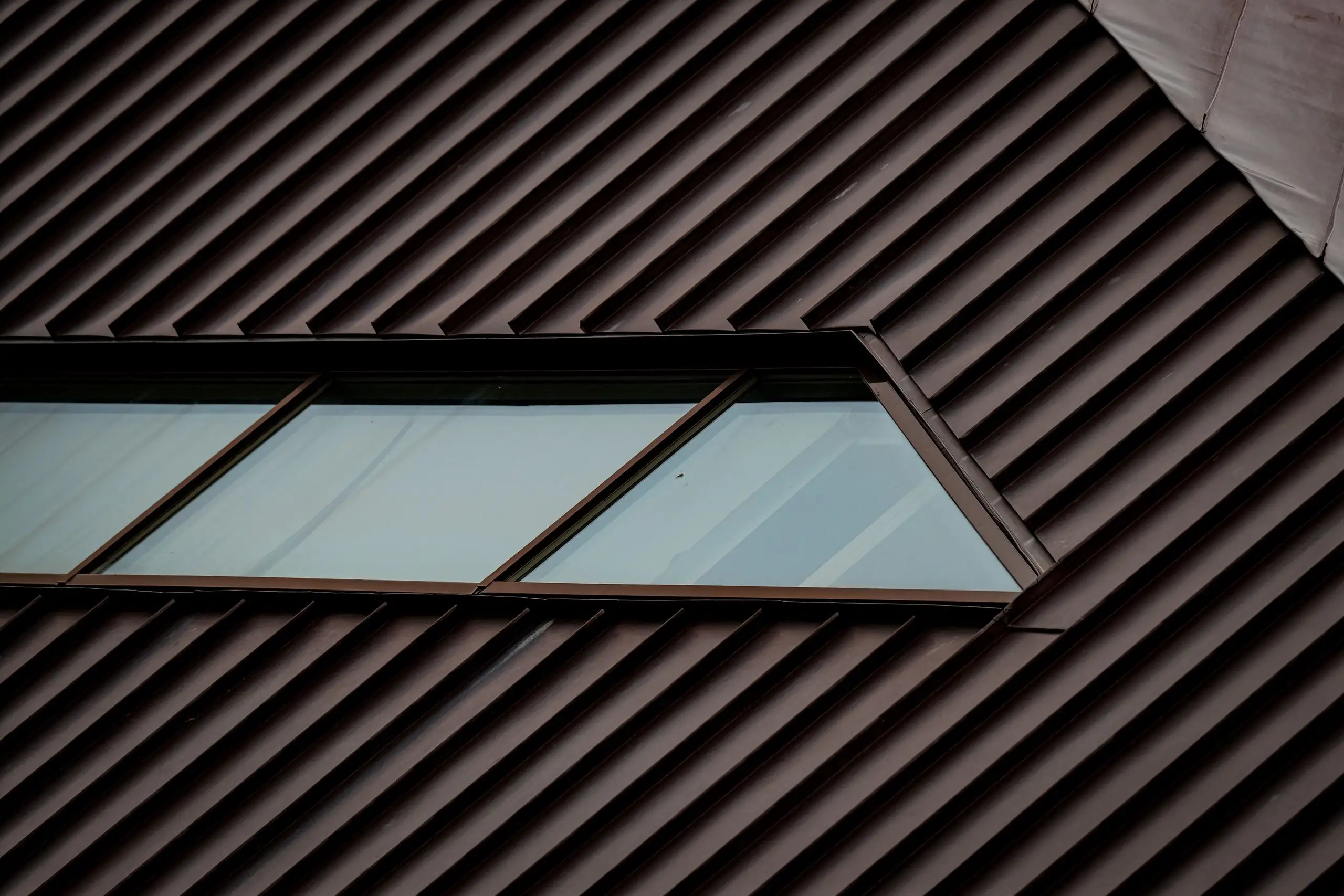 Dark standing seam metal roof in raking light, with a flush skylight set between the seams
