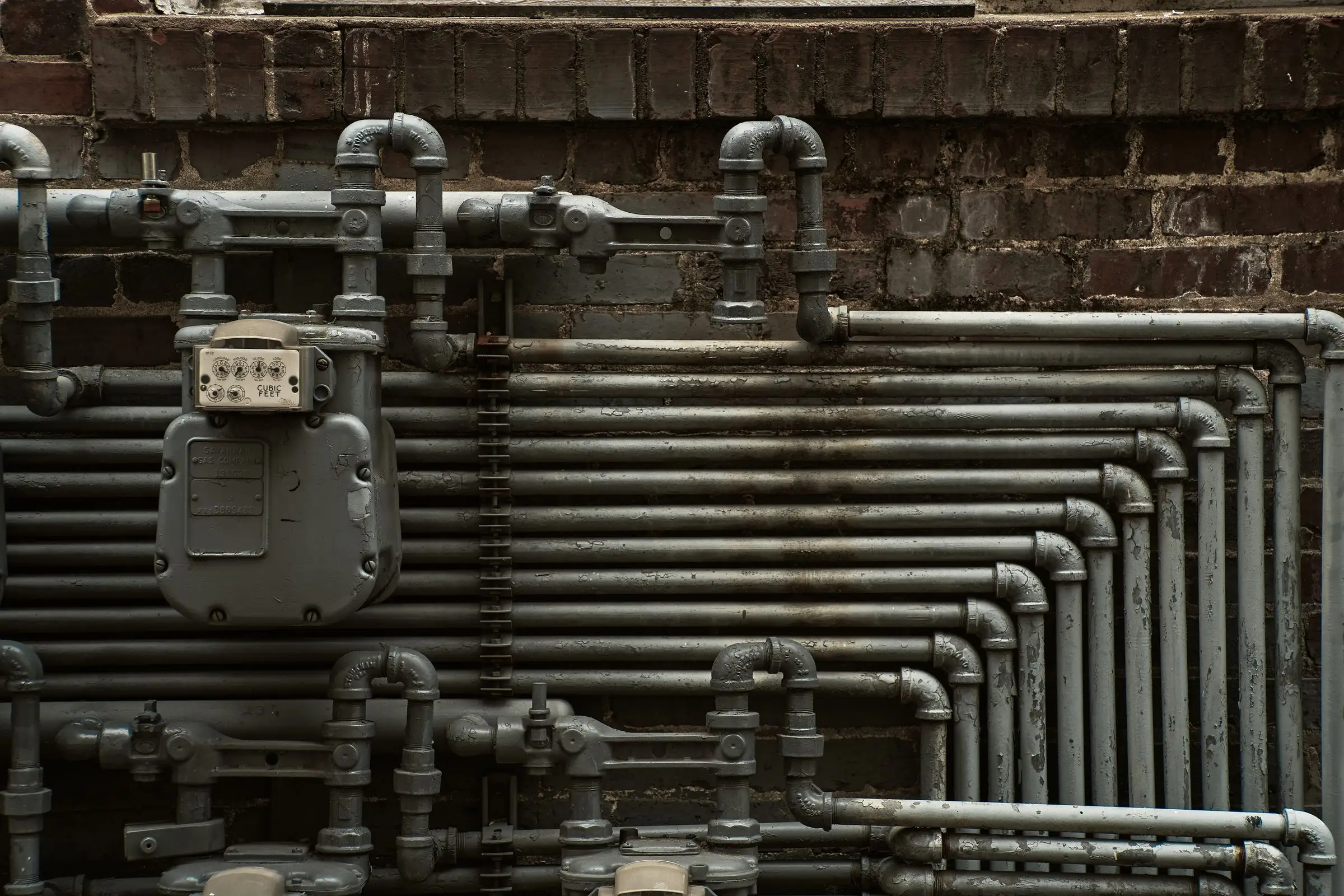 Steel supply pipes and a meter mounted on a brick wall