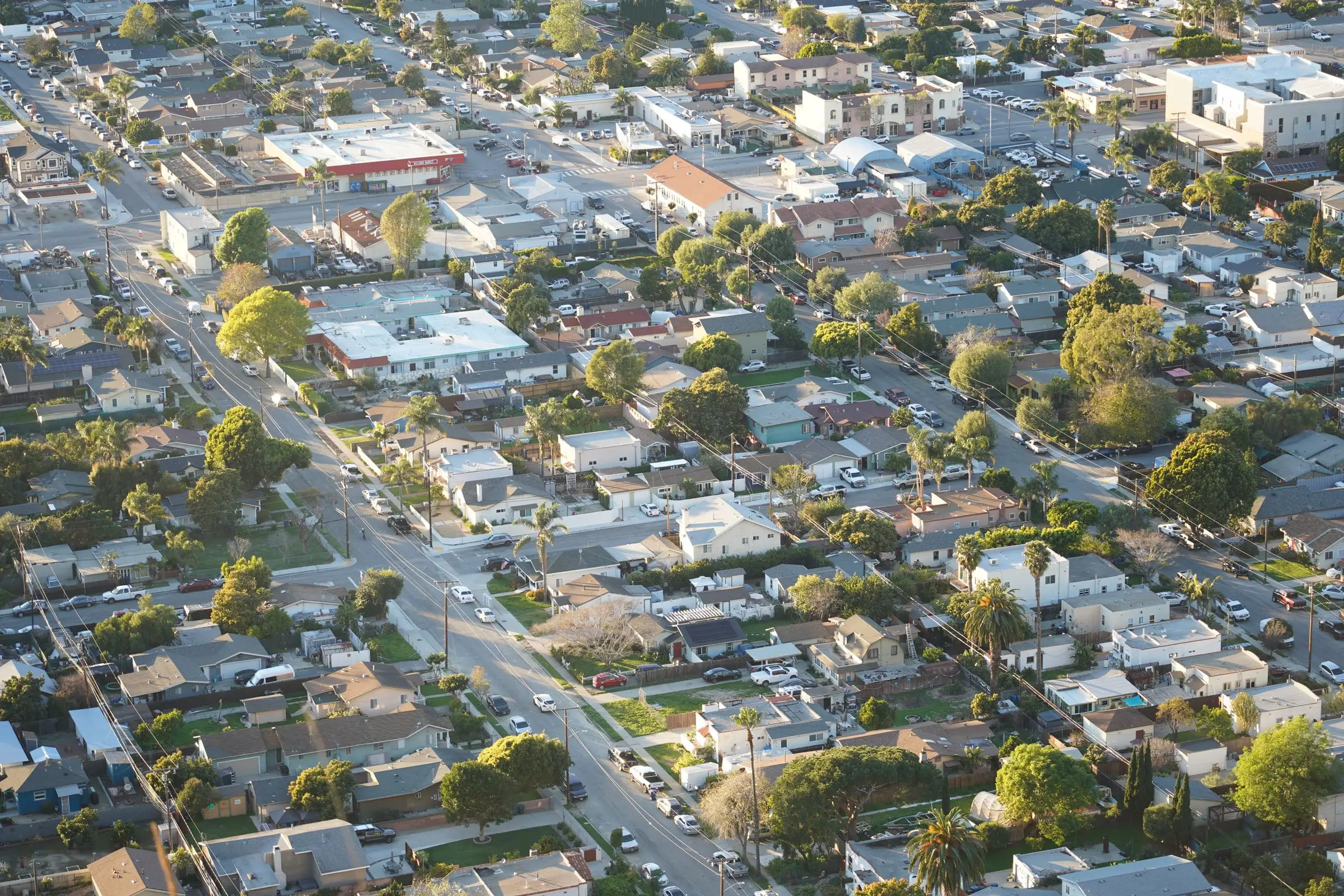 Suburban American rooftops seen from the air in low evening light, streets cutting between them