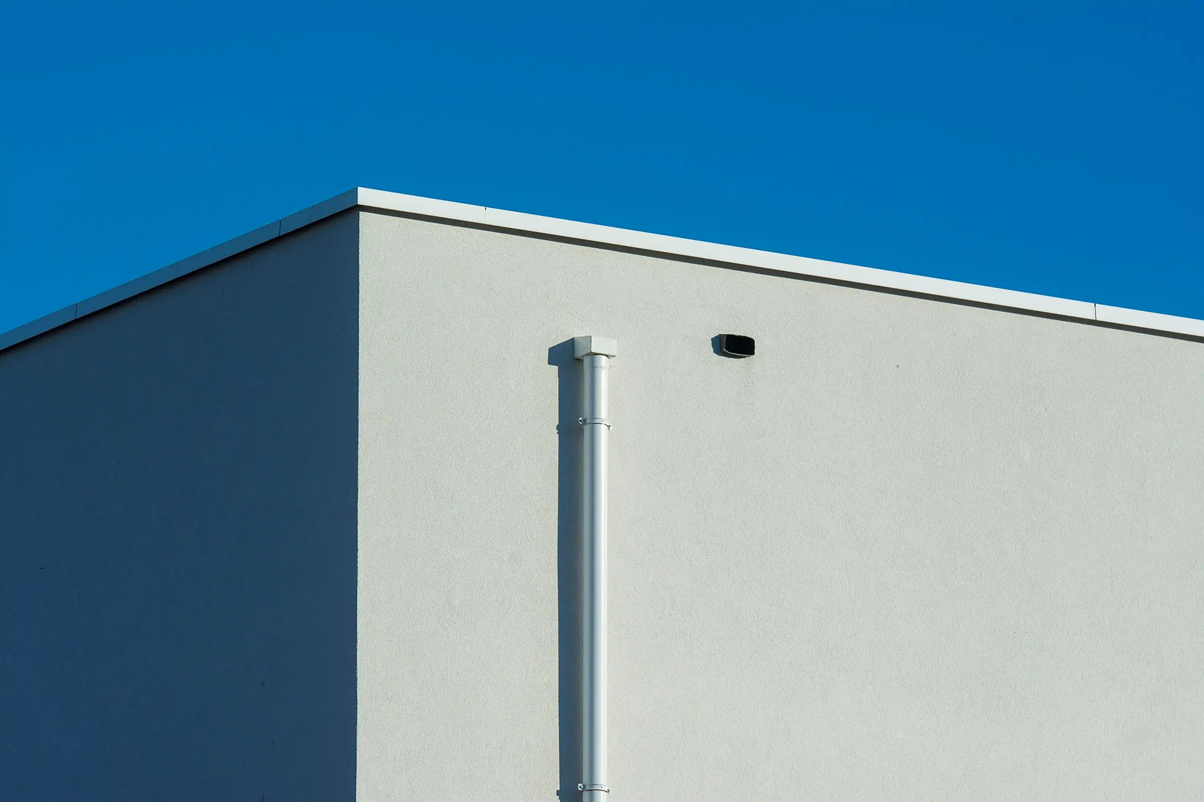 Sunlit building corner with a downpipe running its full height