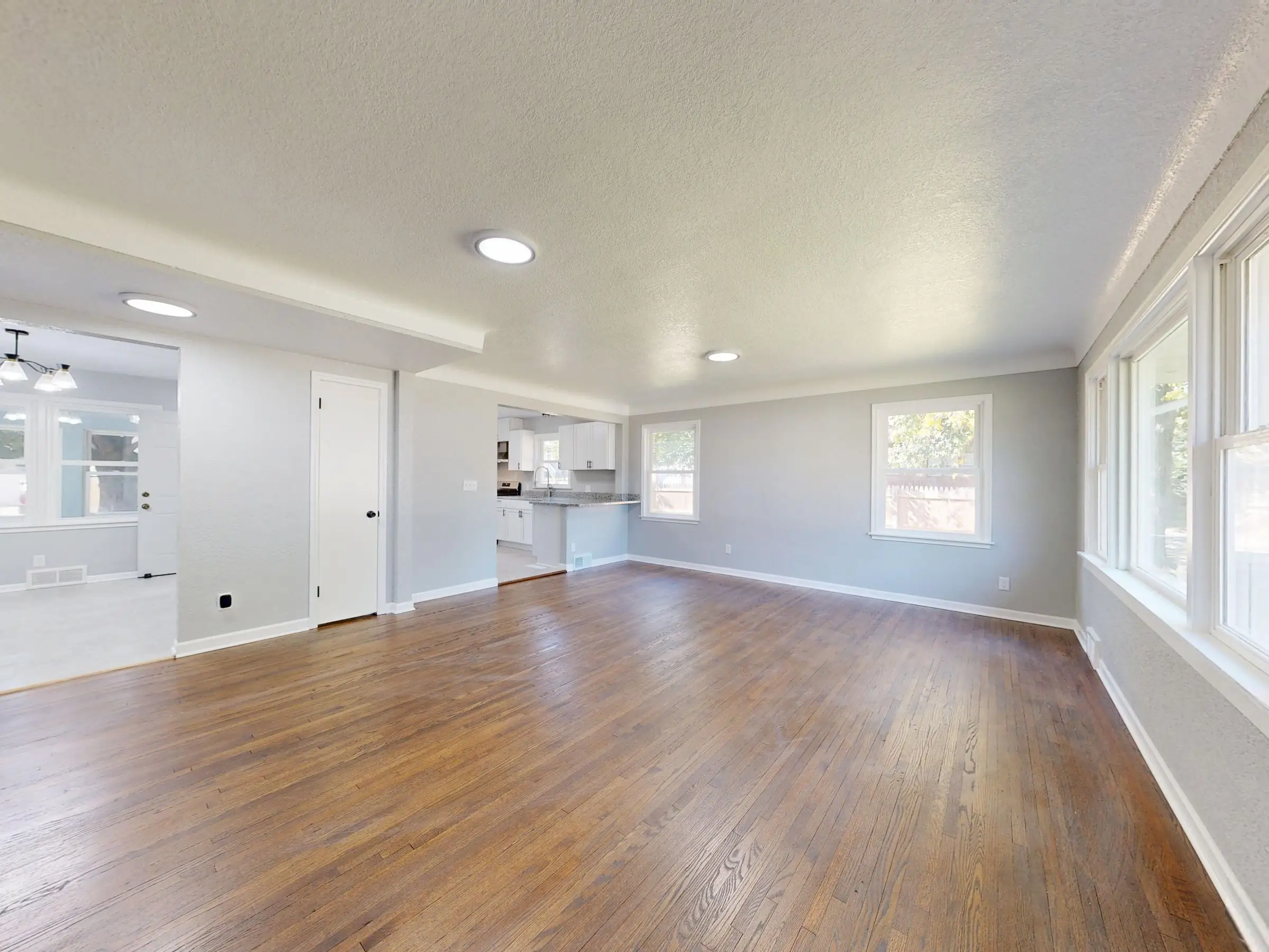 Empty room with a bare wood floor running toward tall windows