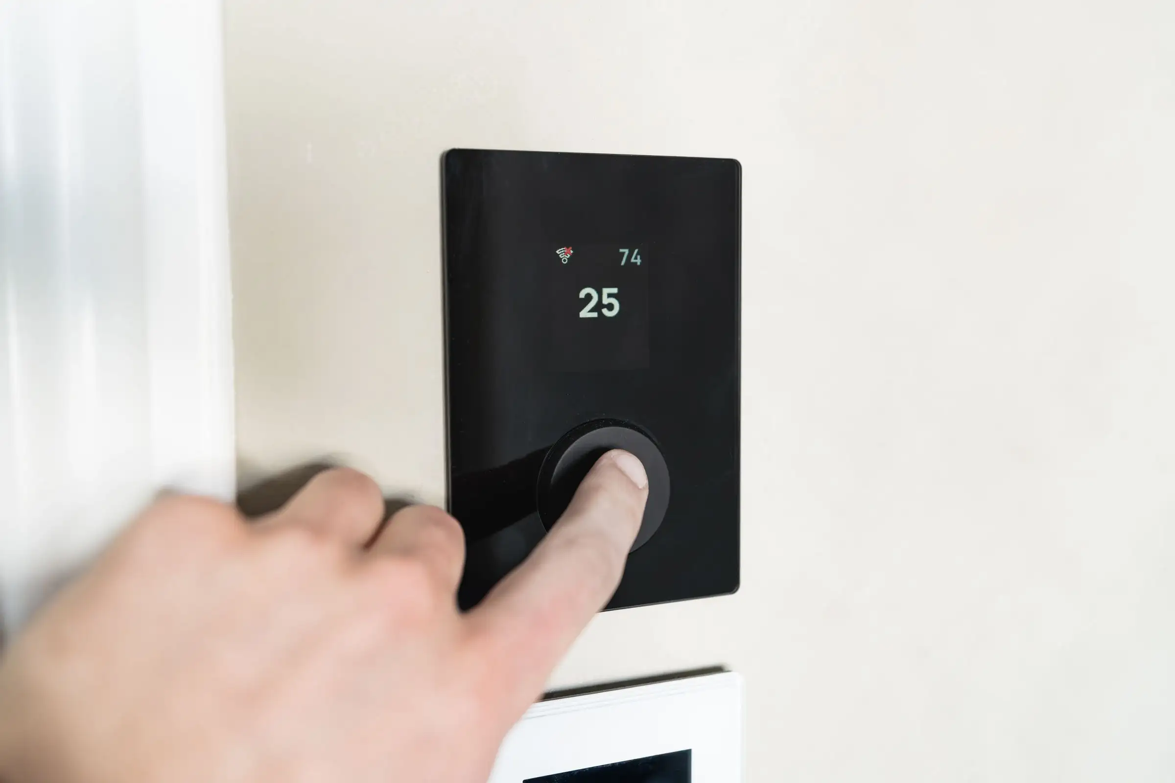 A hand adjusting a plain wall thermostat