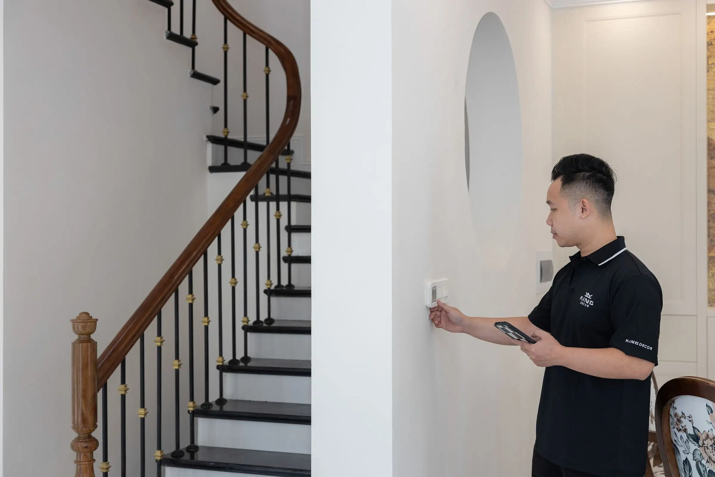A hand setting a wall thermostat beside a staircase
