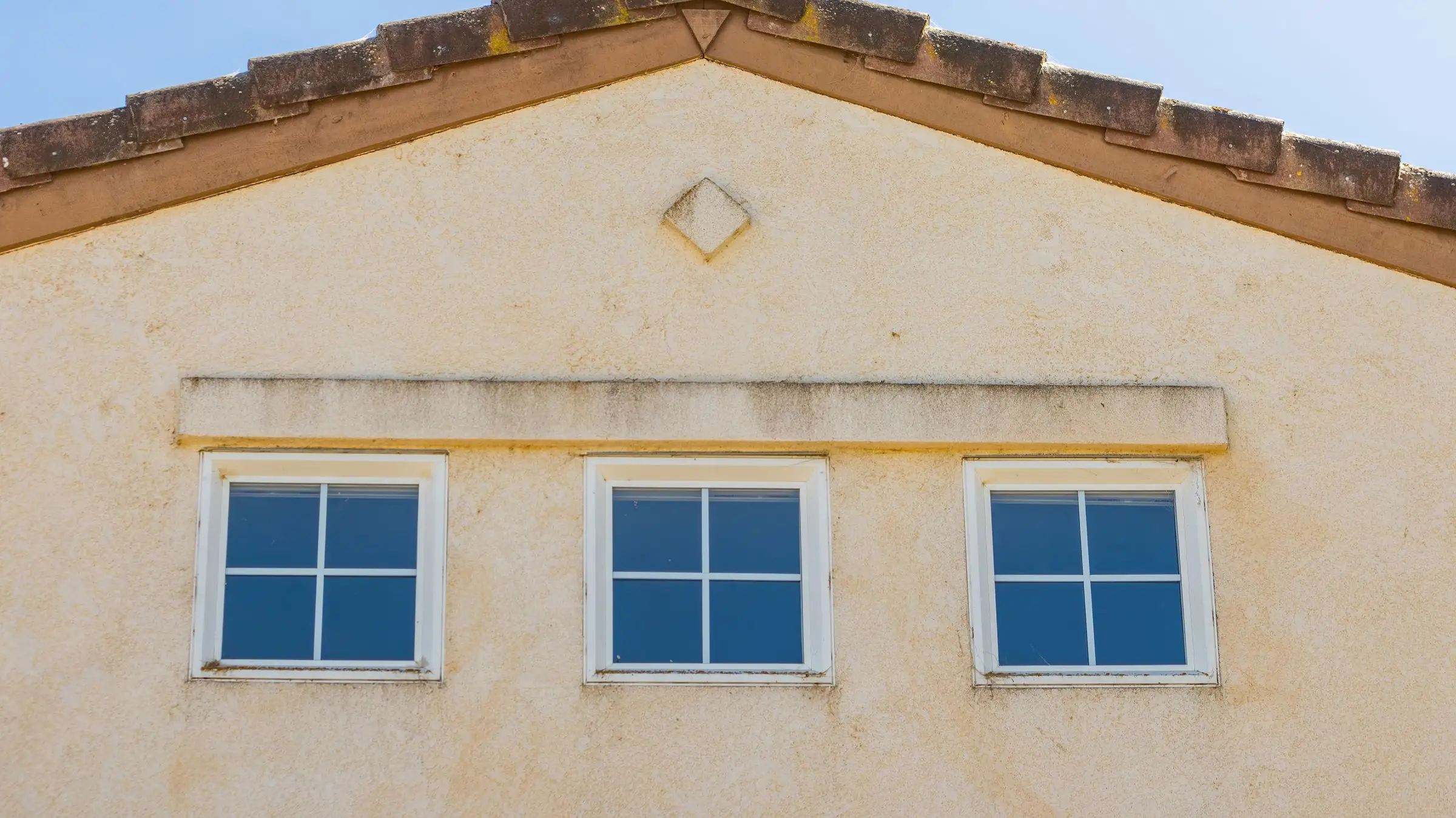Three evenly spaced windows in a plain rendered facade under a gable