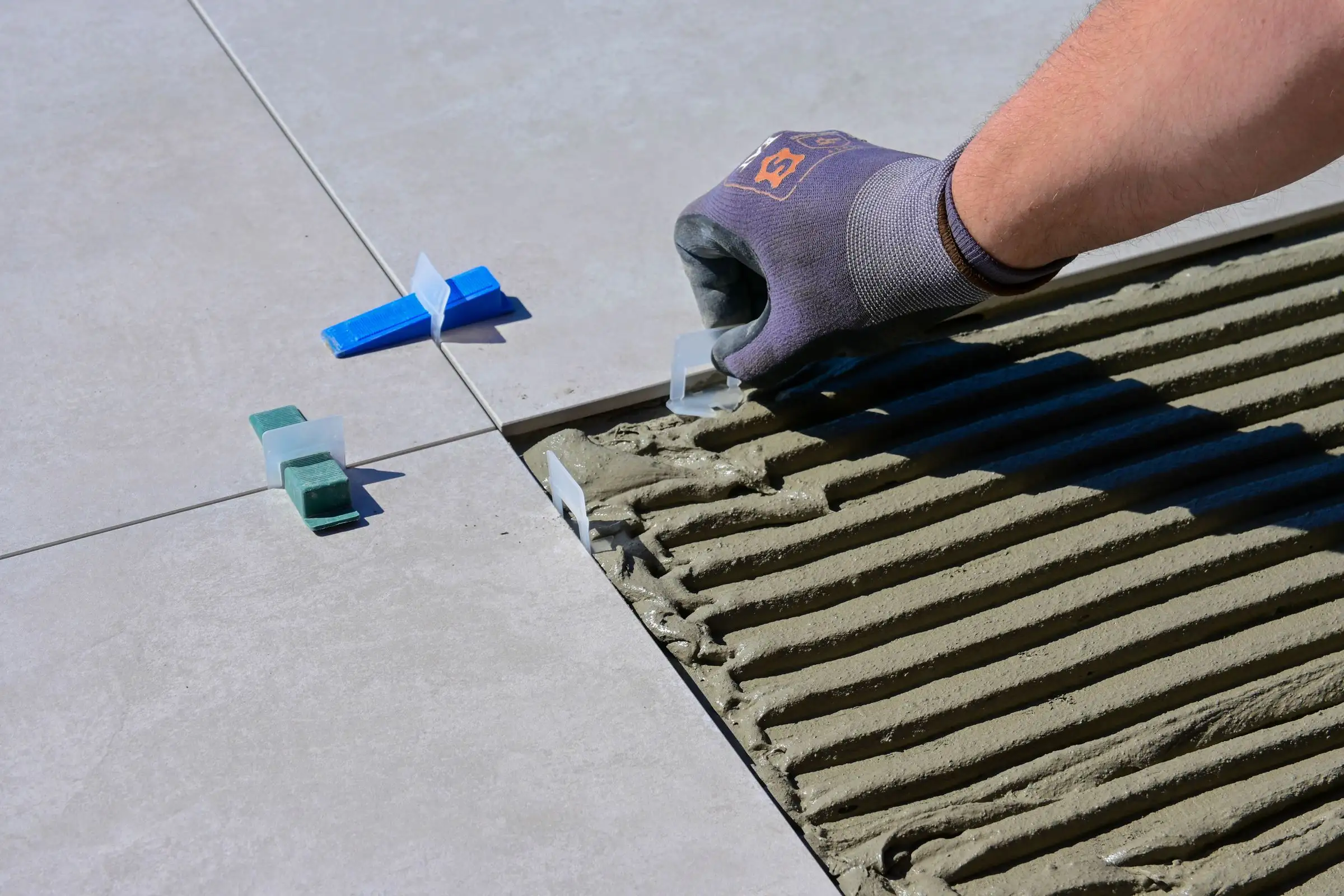 Gloved hand setting a wall tile with plastic levelers and spacers