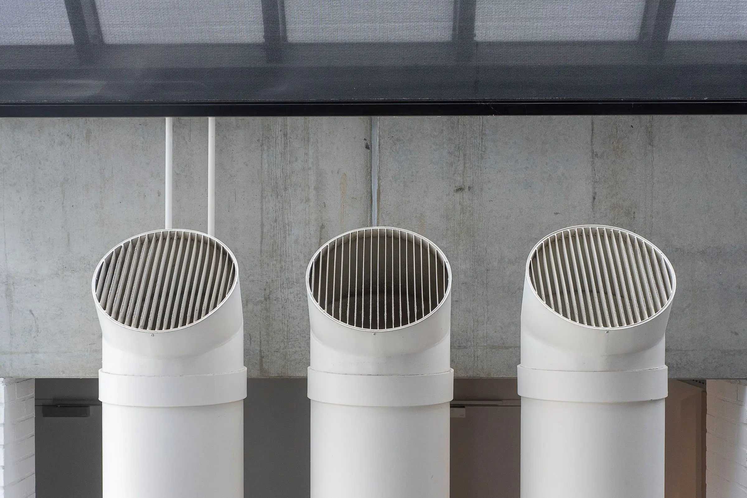 Three white ventilation pipes running side by side down a concrete wall