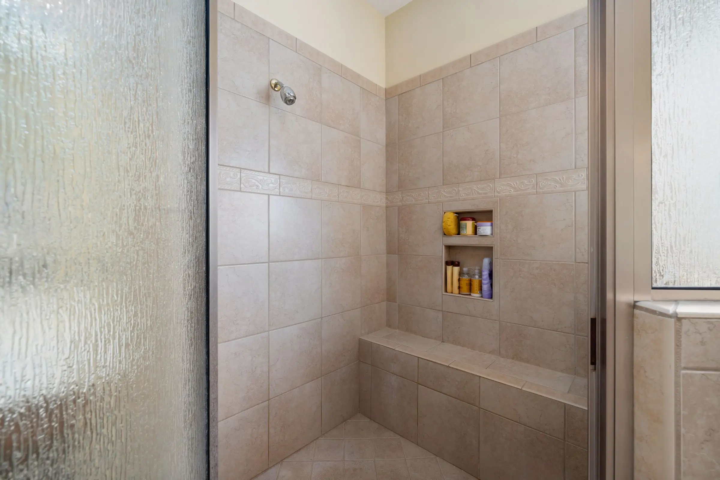 Walk-in shower lined in beige tile with built-in recessed shelves