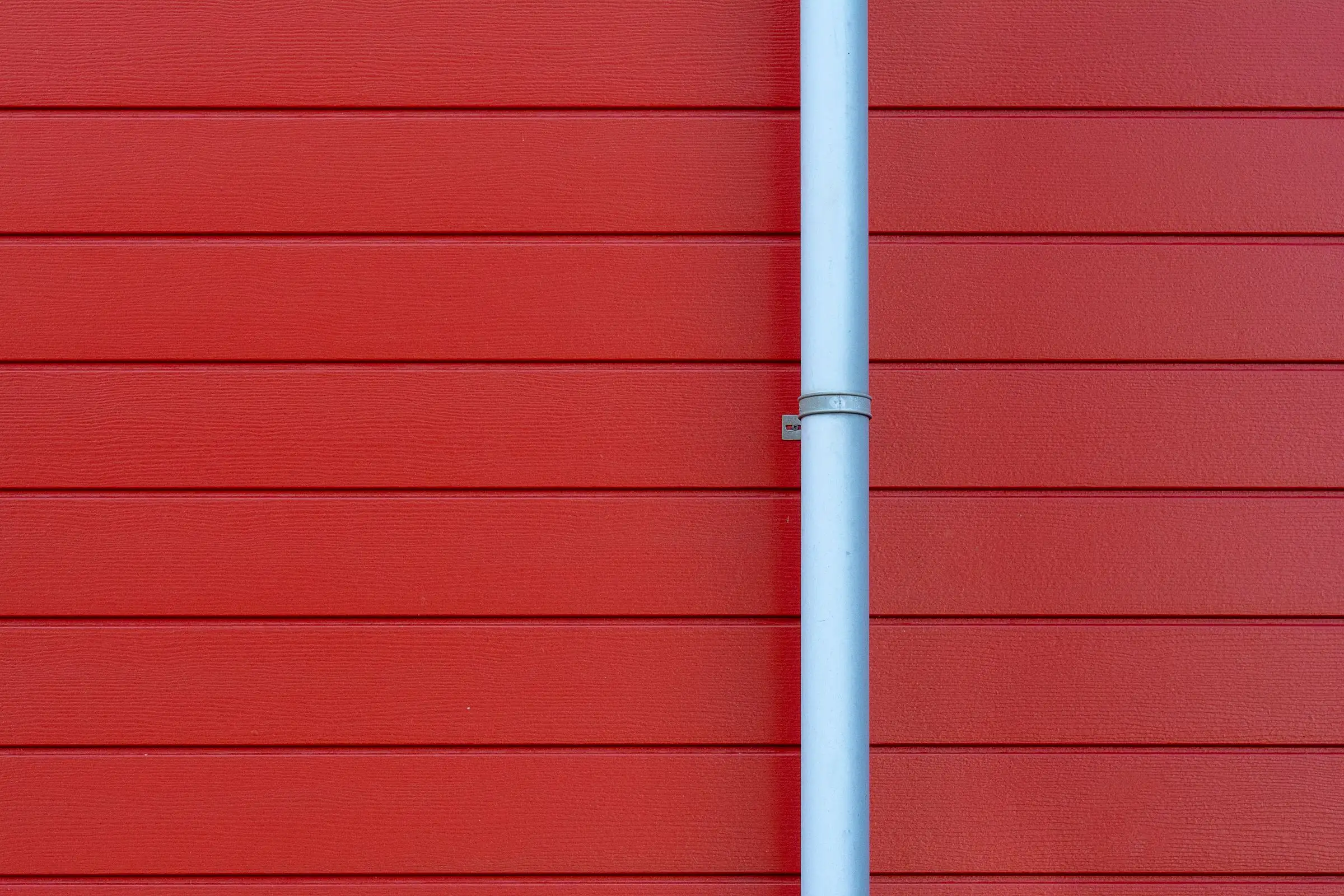 Gouttière blanche courant le long d’un mur rouge