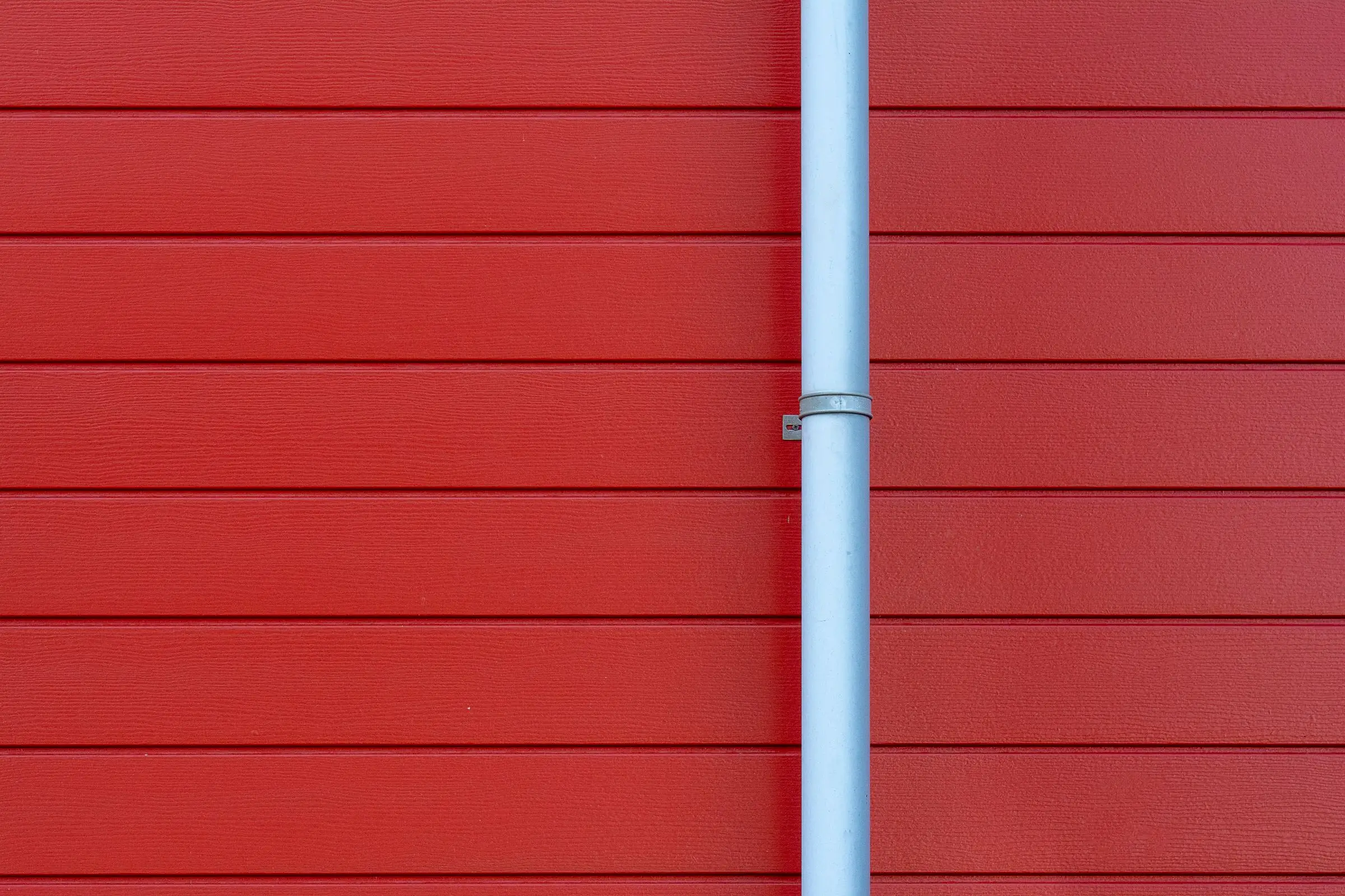 A white gutter and downspout running down a plain red wall